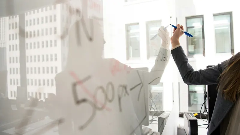 Persona escribiendo un esquema en una pizarra de vidrio